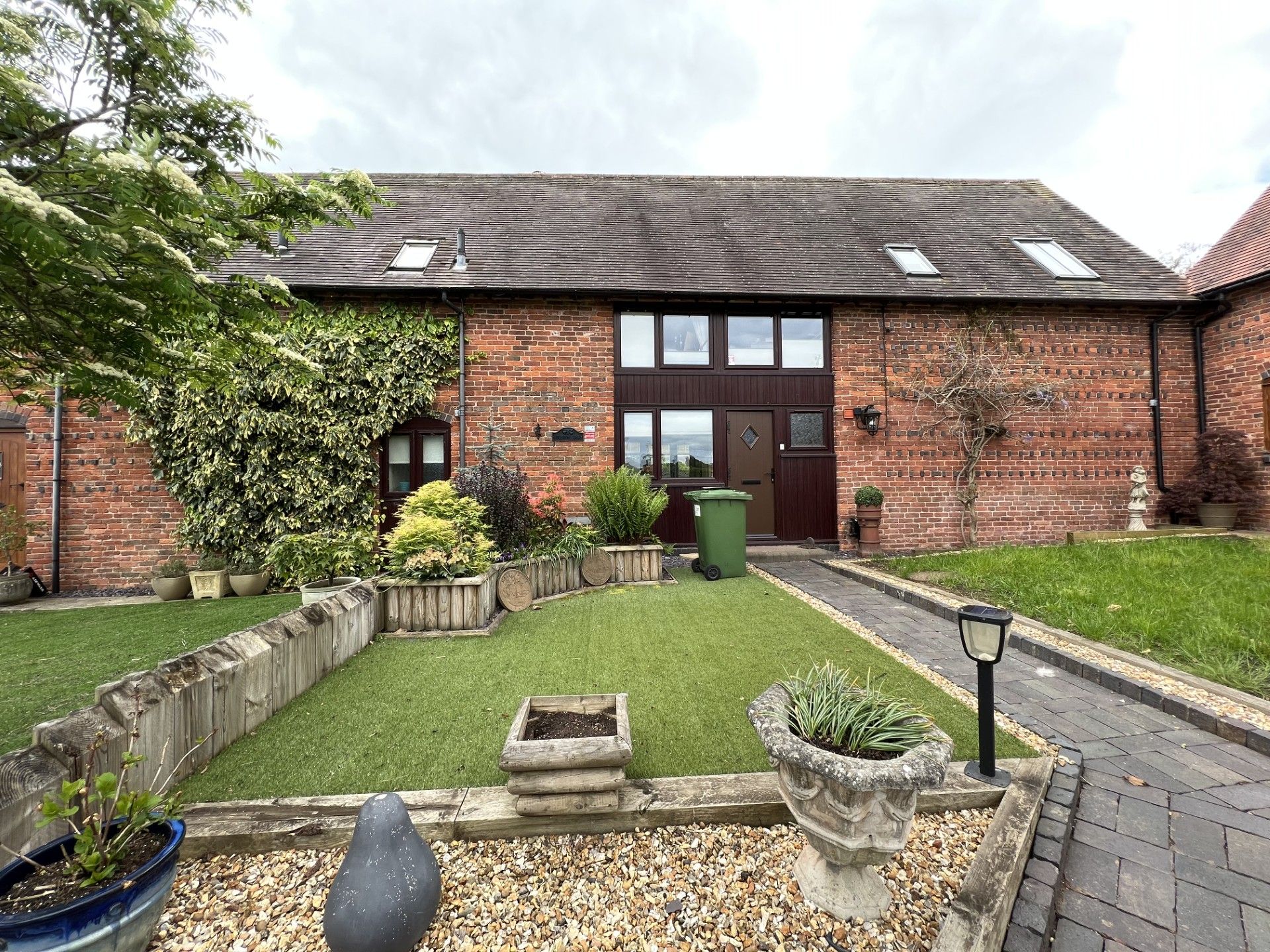 Brick building with a grassy lawn, garden, and pathway leading to the entrance. Overcast sky.