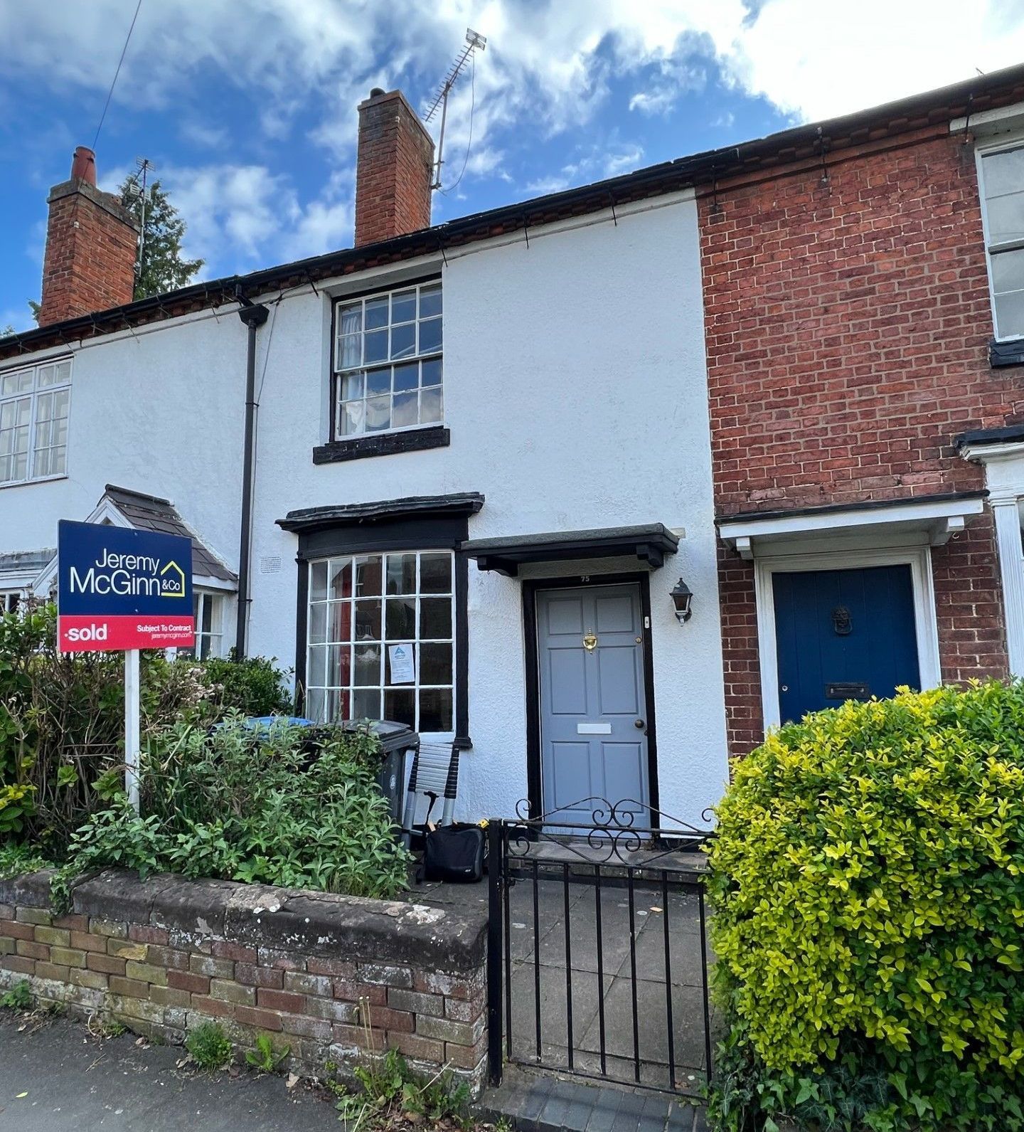 White cottage with black window frames, dark gray door, and a red brick section next to it.