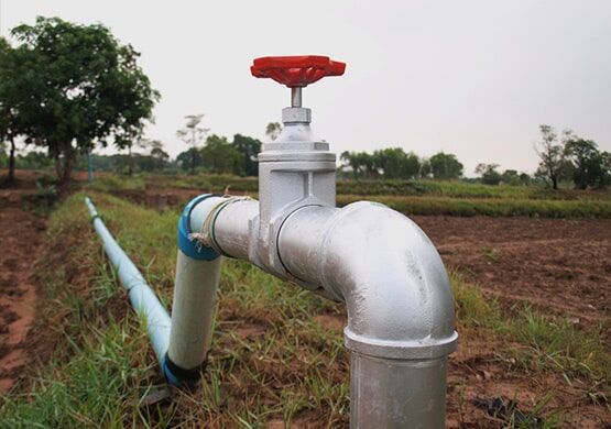 A close up of a water pipe with a red handle in a field.