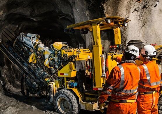 A group of construction workers are standing next to a yellow truck in a tunnel.