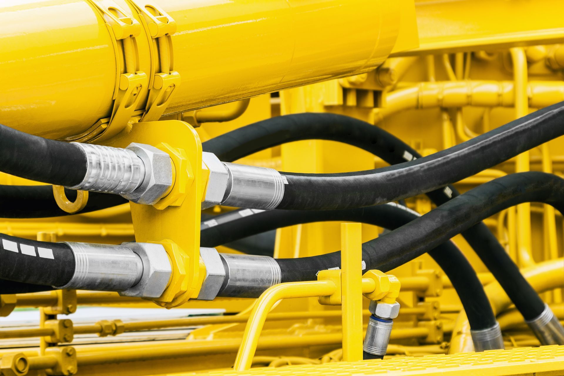 Yellow industrial machinery with black hydraulic hoses and metal fittings close up