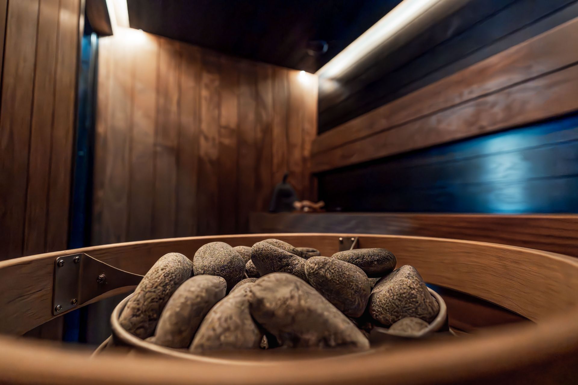 Sauna rivestita in legno con stufa in pietra rotonda e secchio in legno, immersa in una calda luce ambrata.