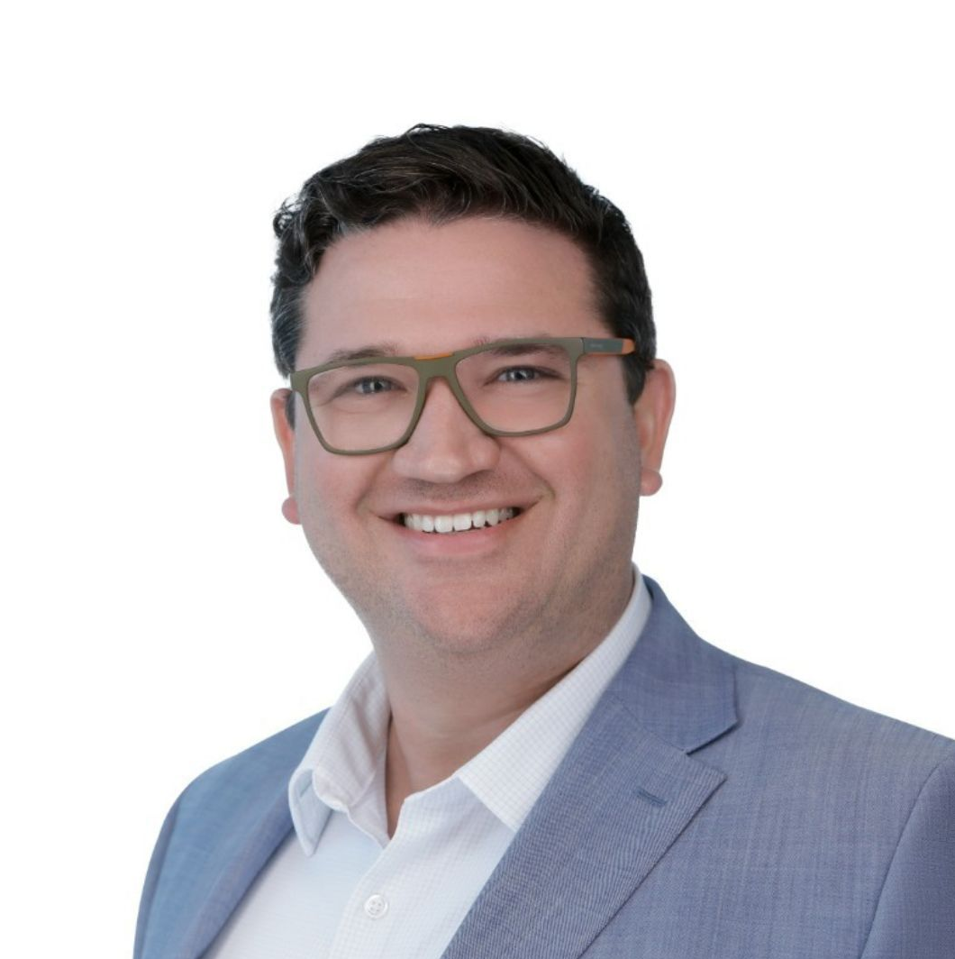 Man with glasses smiles, wearing a blue blazer and white shirt.