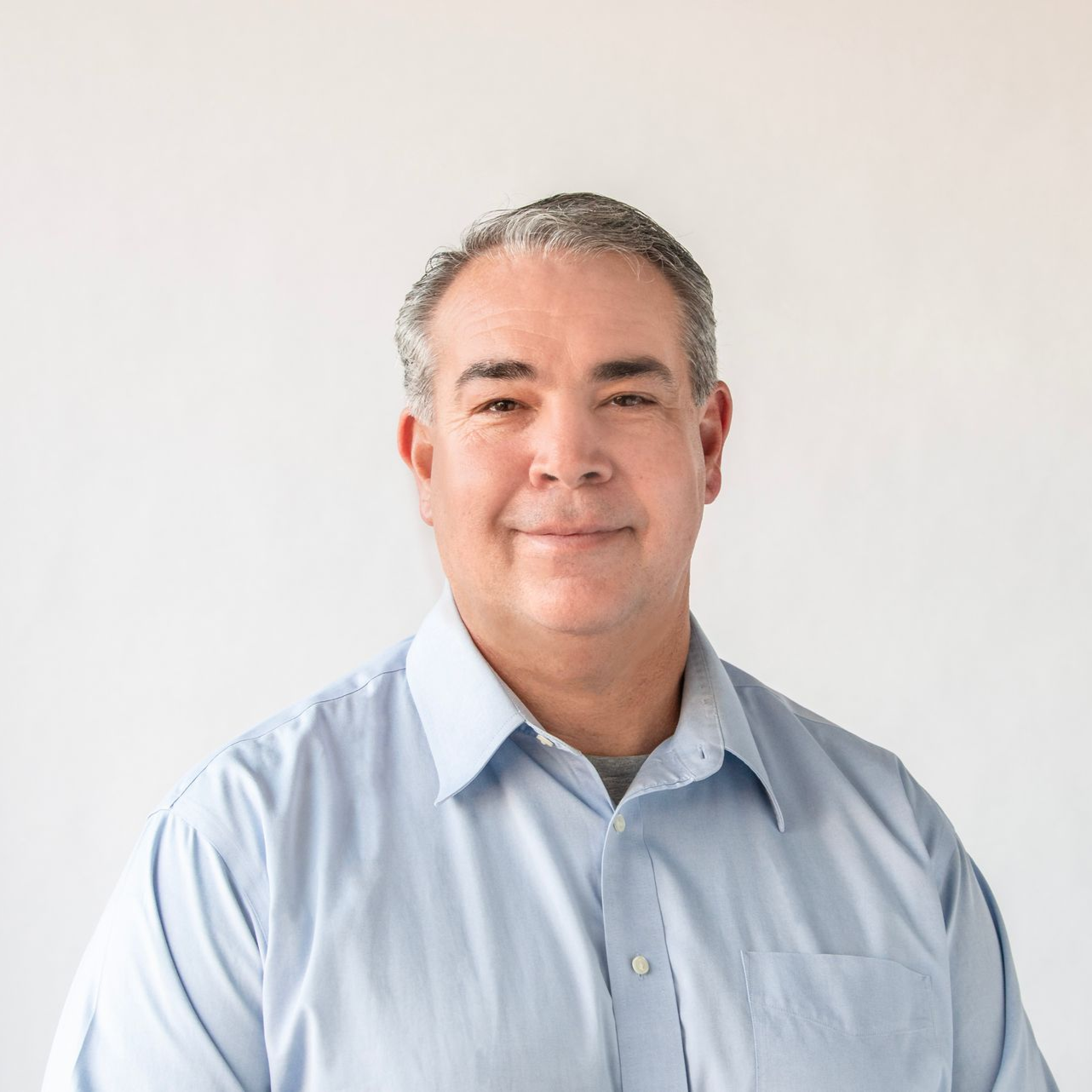 Man with gray hair and a blue shirt smiles against a white backdrop.