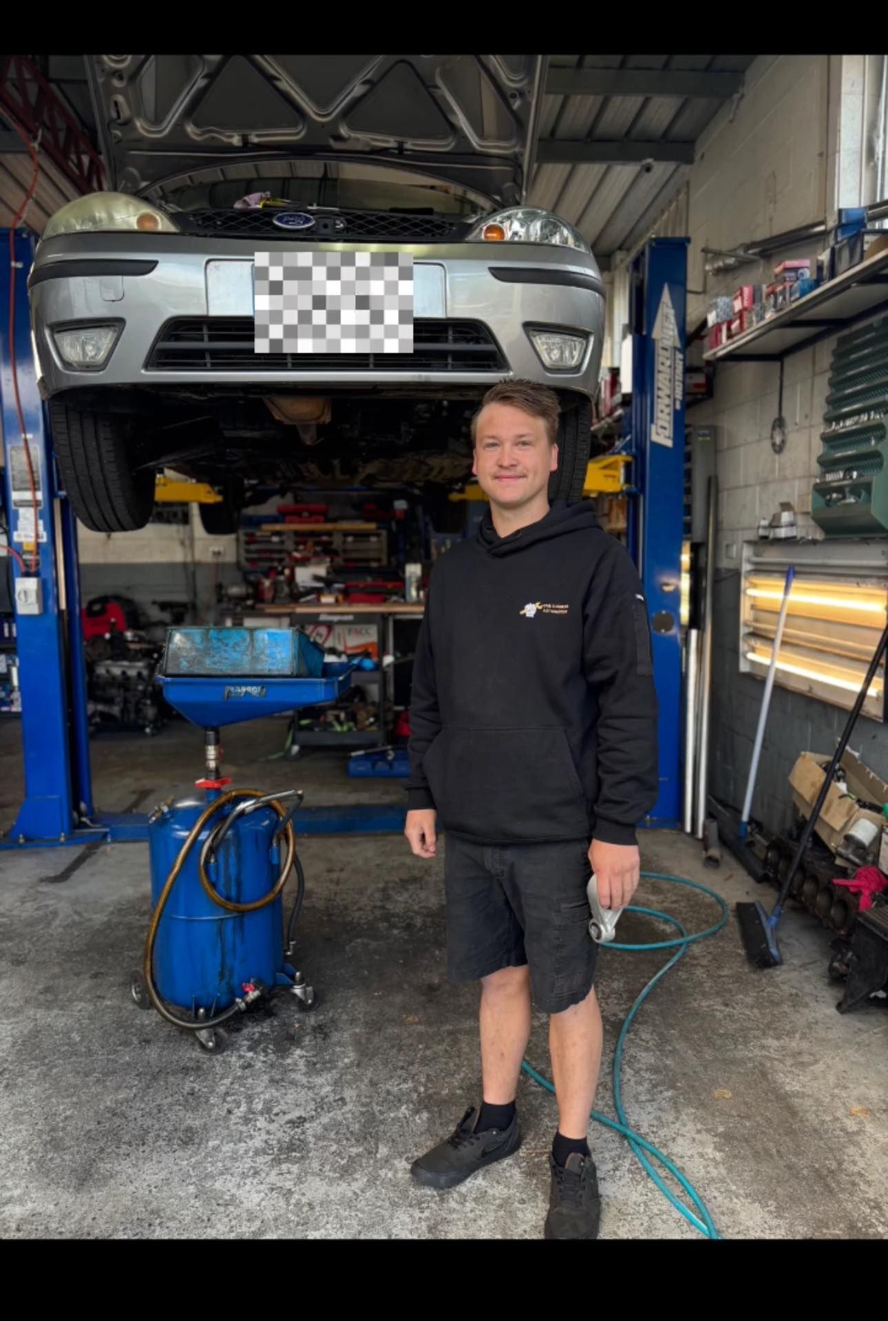 Mechanic Standing in an Auto Shop Beside a Car Raised on a Lift — Van Diemen's Automotive & Electrical Repairs In Bellerive, TAS