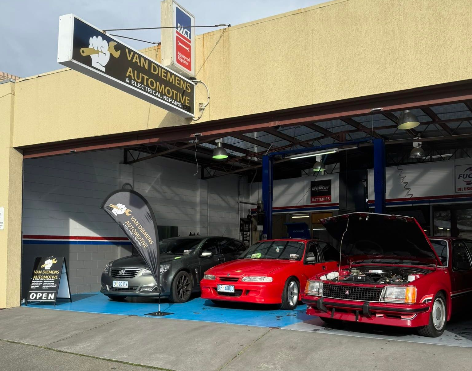 Car Dealership Showroom With A Gray Car, Red Car, And Red SUV Parked Outside The Open Bay — Van Diemen's Automotive & Electrical Repairs In Bellerive, TAS