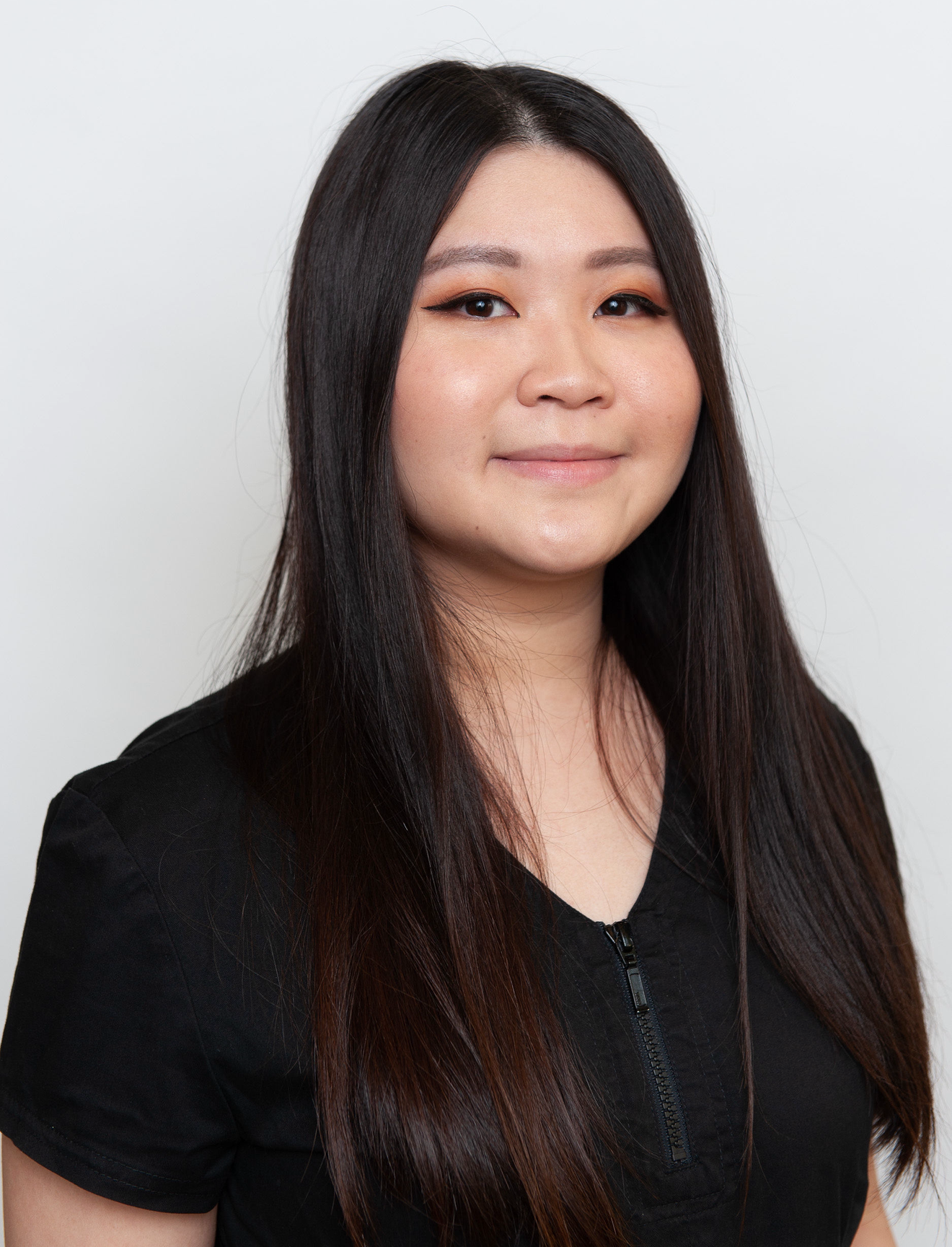 Woman with dark hair smiles in front of a white background. She wears a black top and name tag.