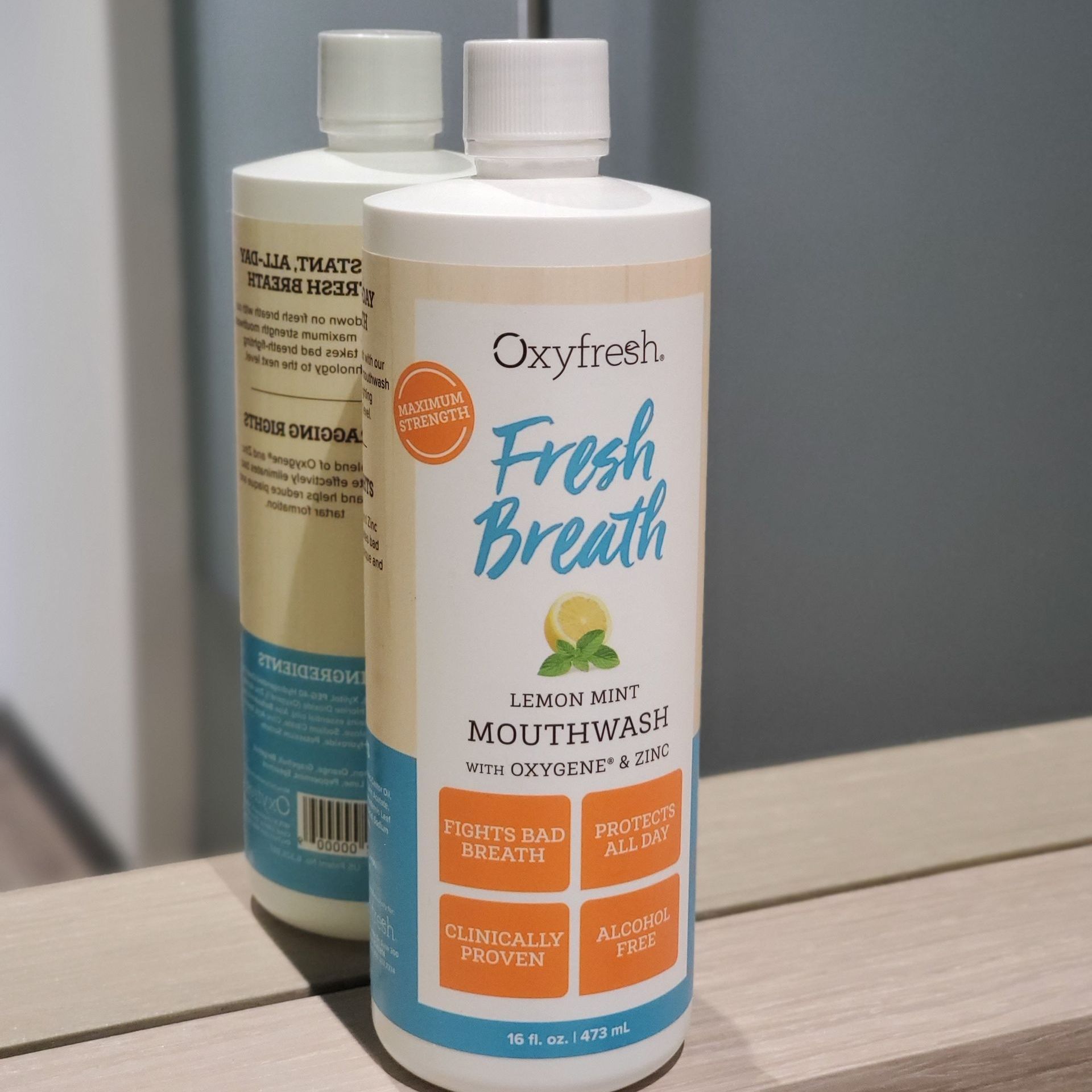 Two bottles of Oxyfresh Fresh Breath lemon-mint mouthwash sitting on a reflective surface.