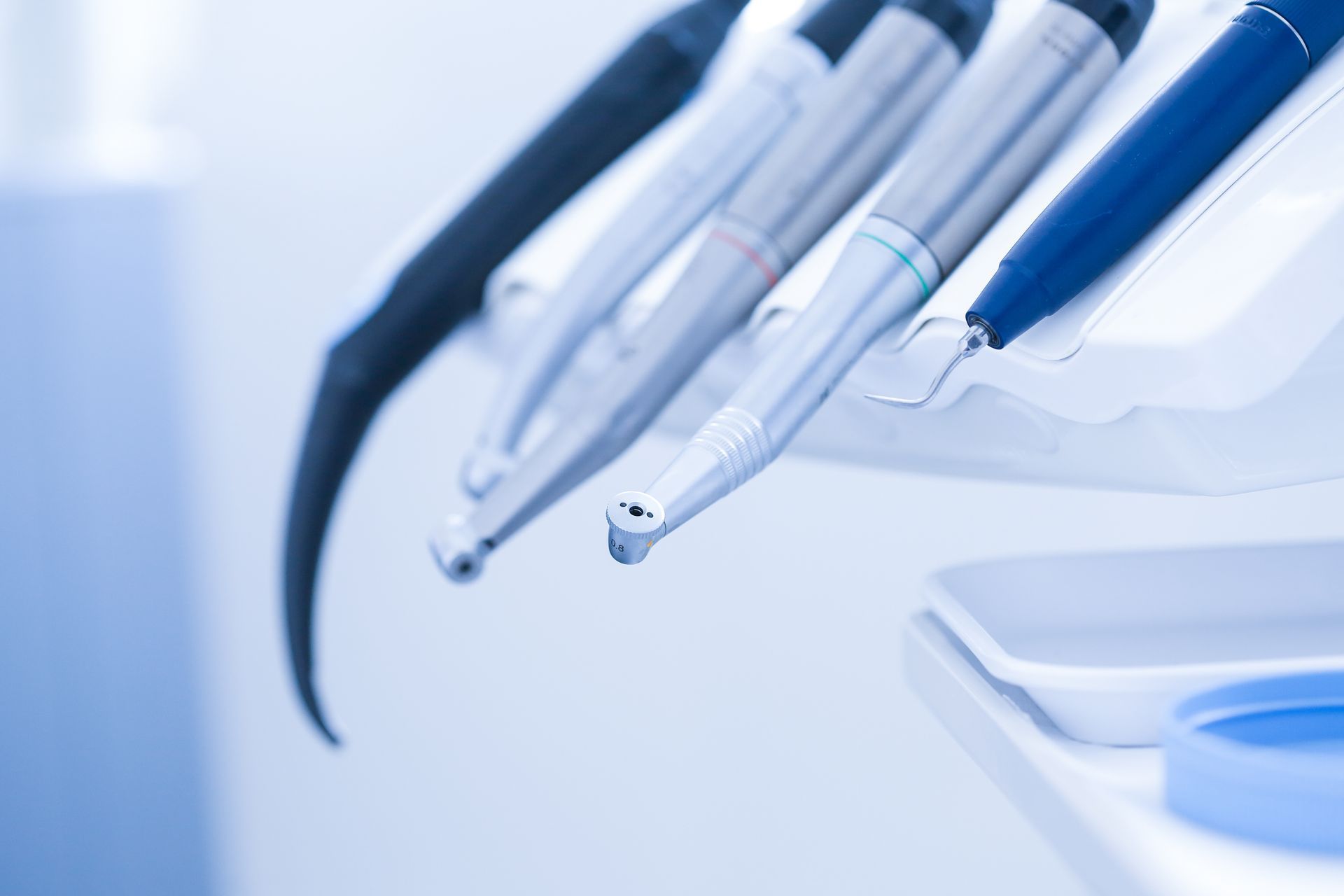 Dental tools, including a drill, on a dentist's tray, close-up with a blue-toned filter.