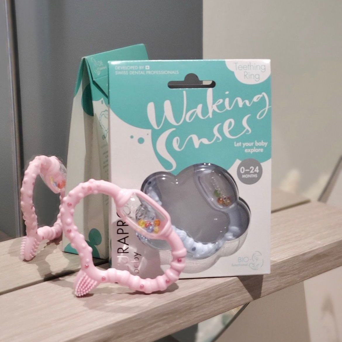 Pink baby teether and packaged teething toy, both on a shelf.