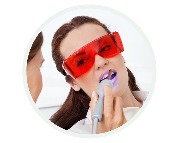 Woman in red glasses has dental work done with a blue light, in a dental office.