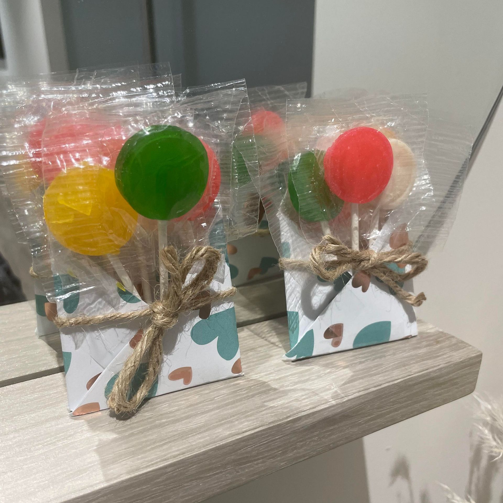 Two lollipop bouquets in patterned boxes, tied with twine. Each has colorful lollipops wrapped in cellophane.