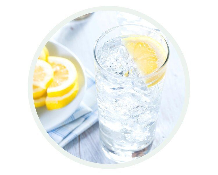 Glass of ice water with lemon wedge, lemon slices on a plate.