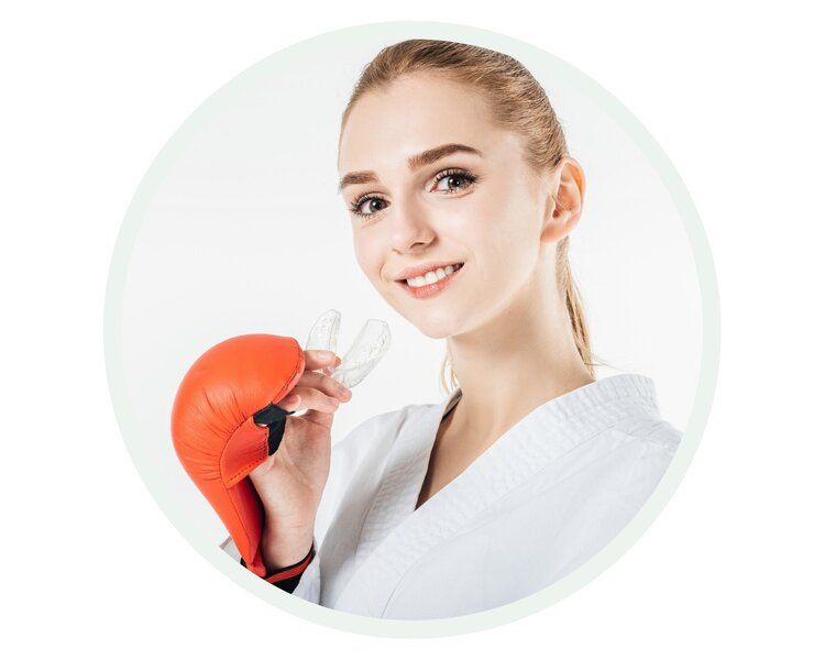 Woman in karate uniform with red boxing glove and mouthguard, smiling.
