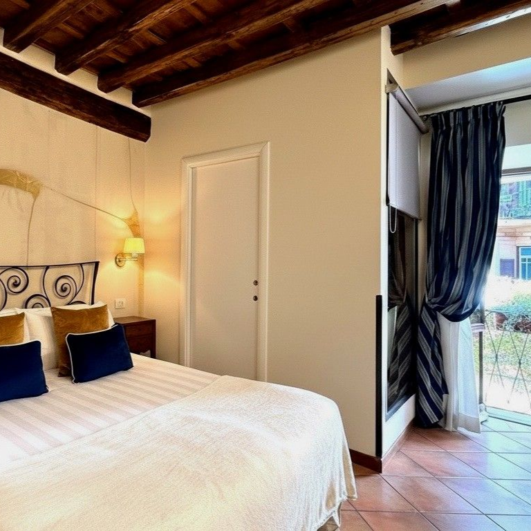 Chambre avec un lit, une porte blanche et un balcon avec des rideaux à rayures. Poutres apparentes au plafond.