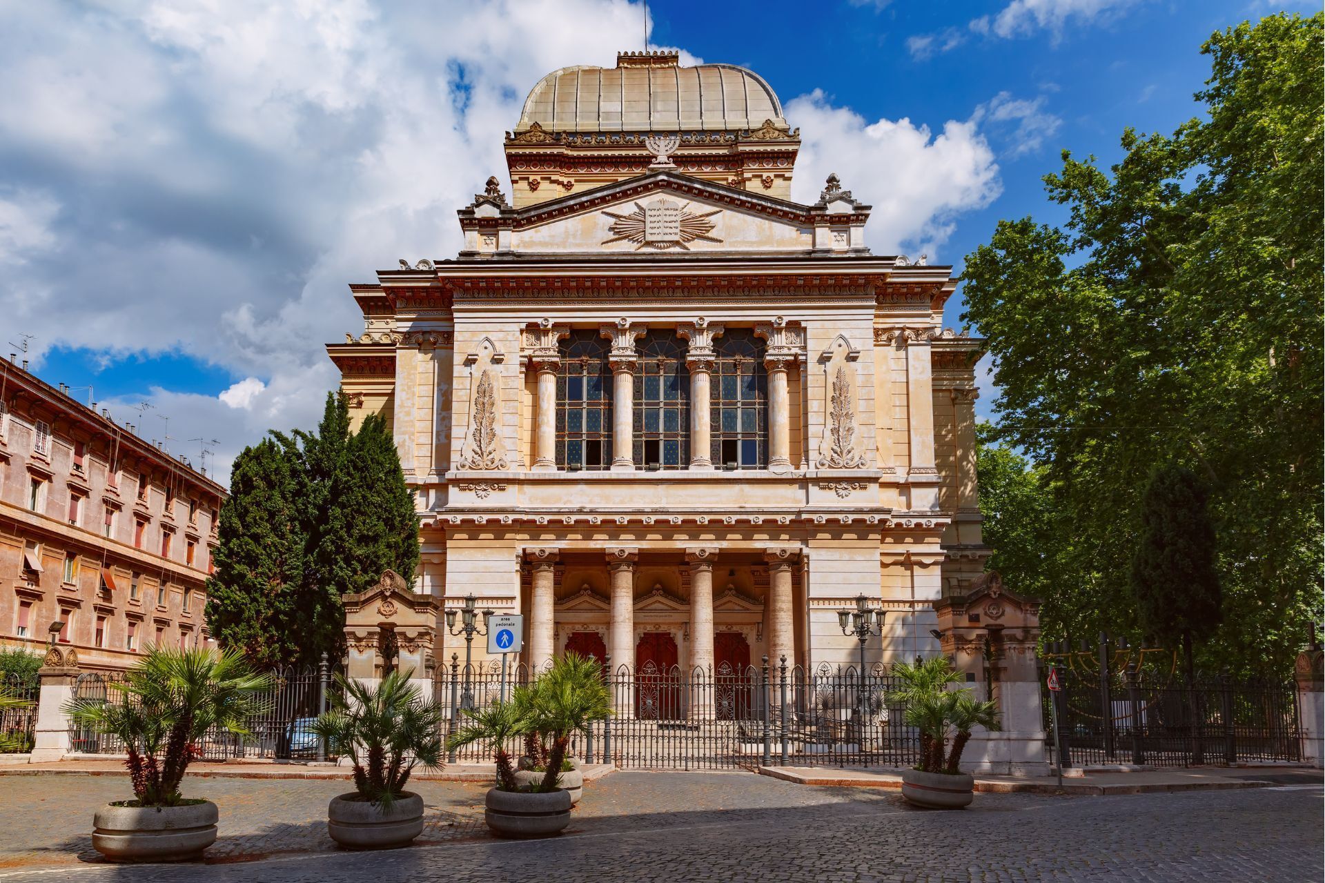 Sinagoga beige con cupola a Roma, Italia, con colonne, finestre ad arco e una piazza acciottolata.