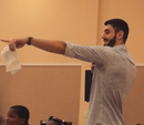Man with beard, holding paper, points to left. Light shirt. Inside setting.