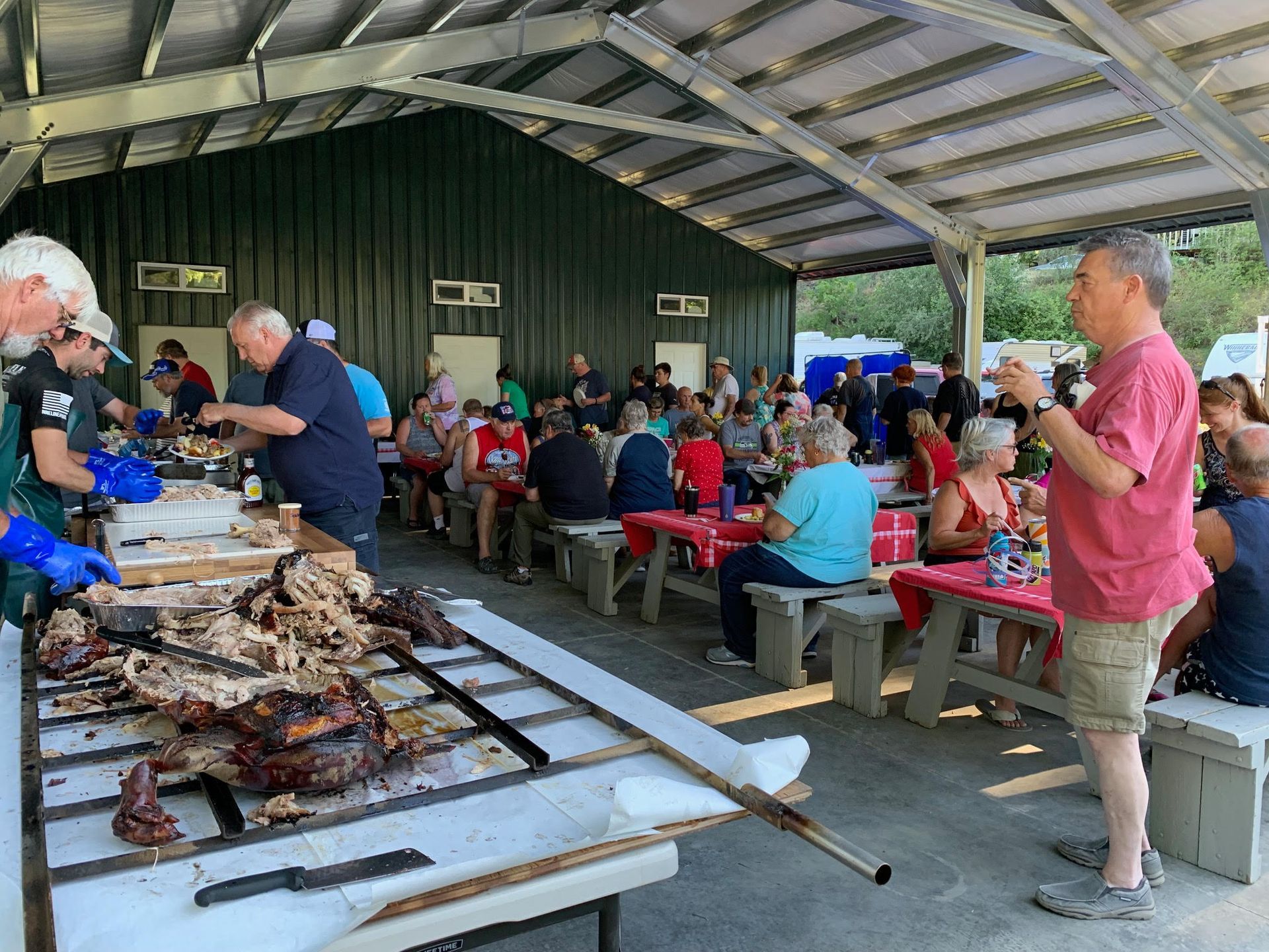 People at a picnic under a covered pavilion, food being served from large tables.