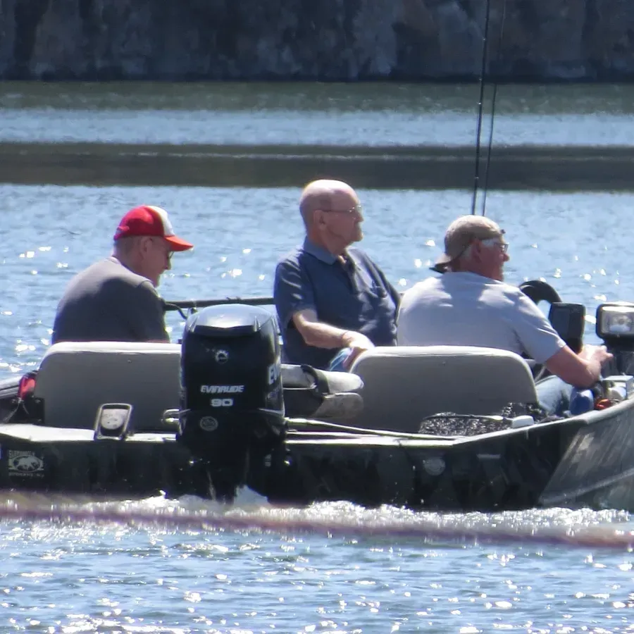 Three people on a boat with a motor on a lake. One wears a red hat, others have fishing rods.