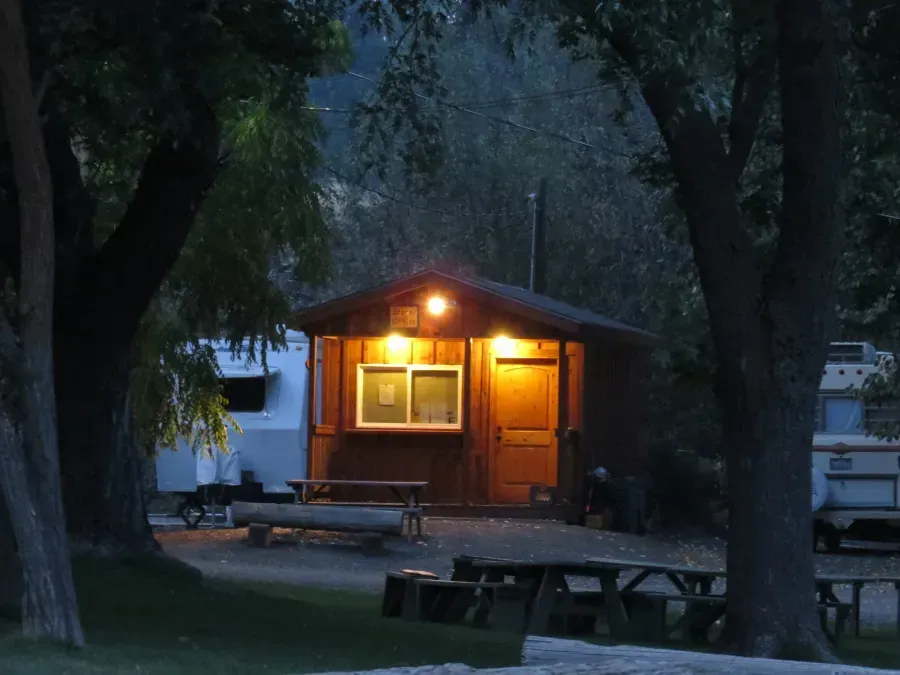 Cabin lit at night, picnic tables, RVs in background, trees frame the scene.