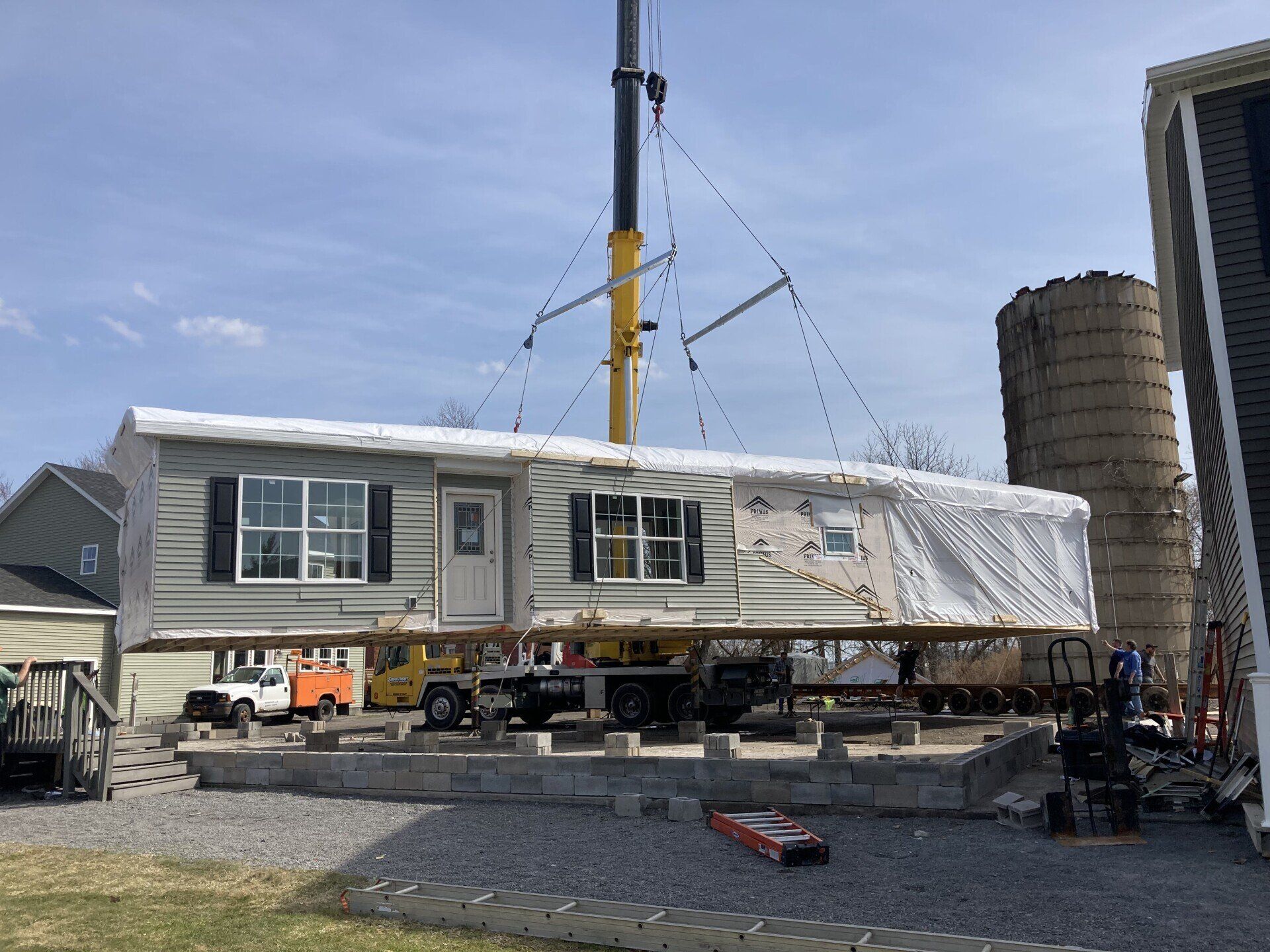 Mobile home suspended in air by crane, being moved. Bright day, rural setting.
