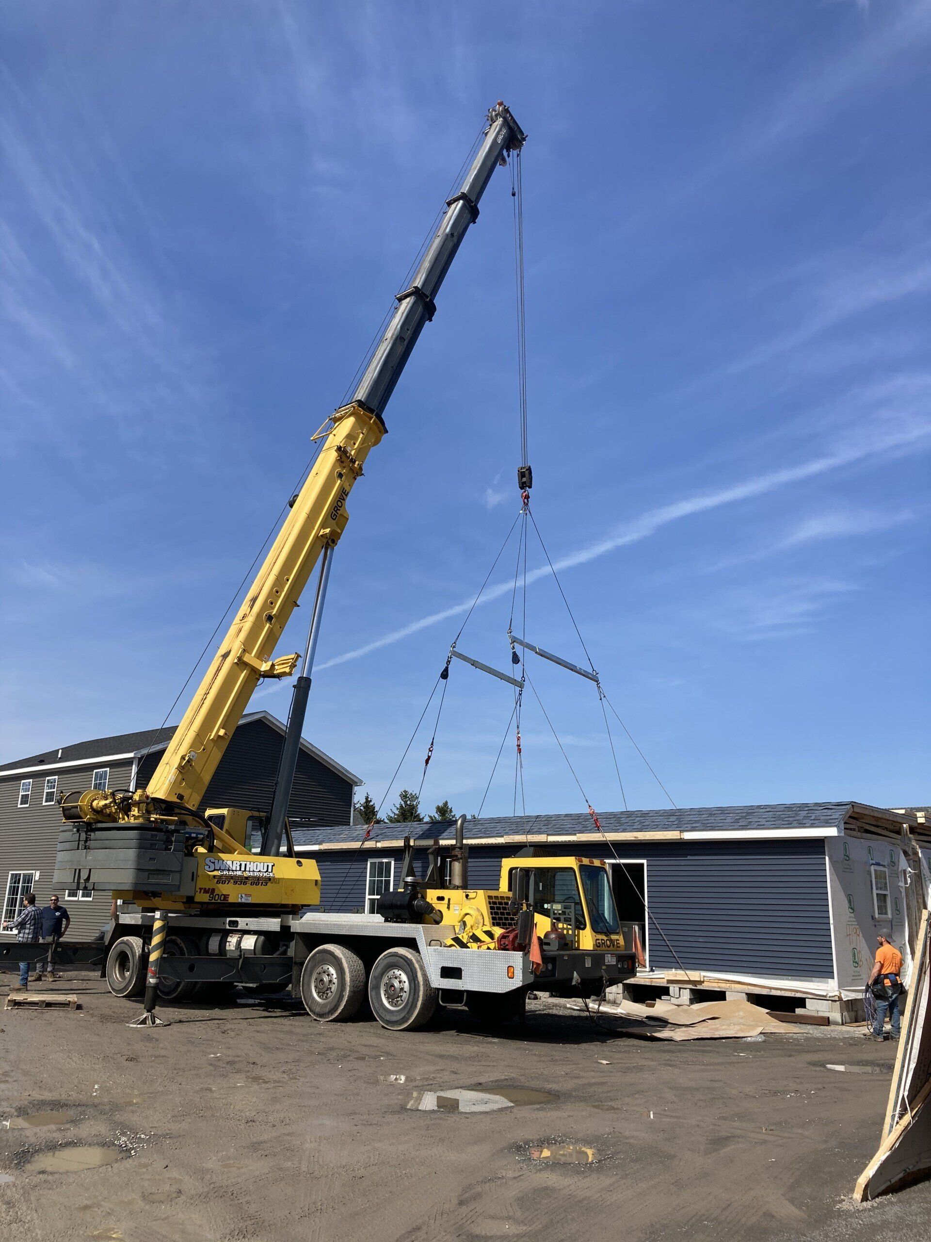 Yellow crane lifting metal beams at a construction site with blue siding and a clear sky.