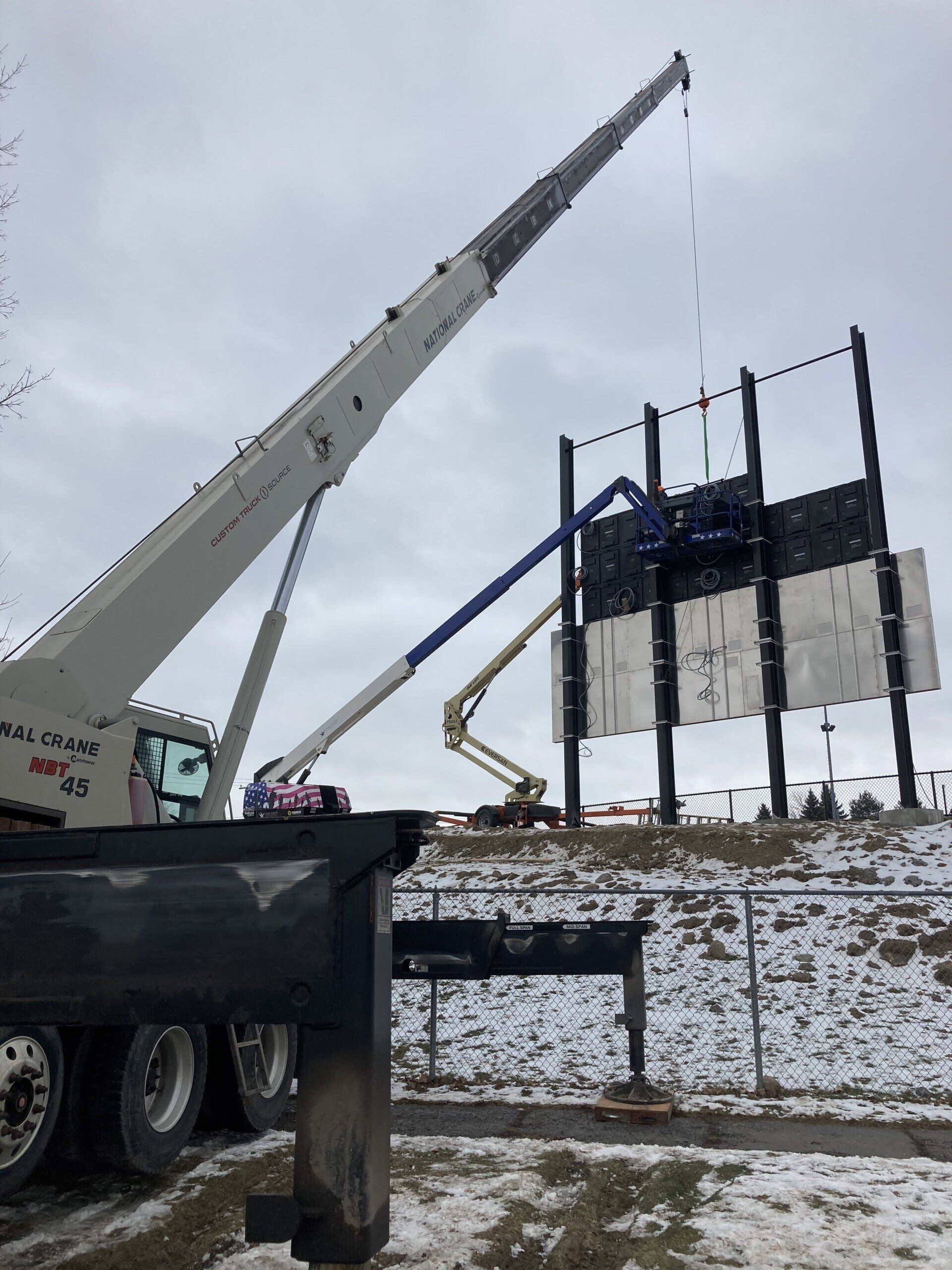 A large crane is lifting a large billboard in the snow.