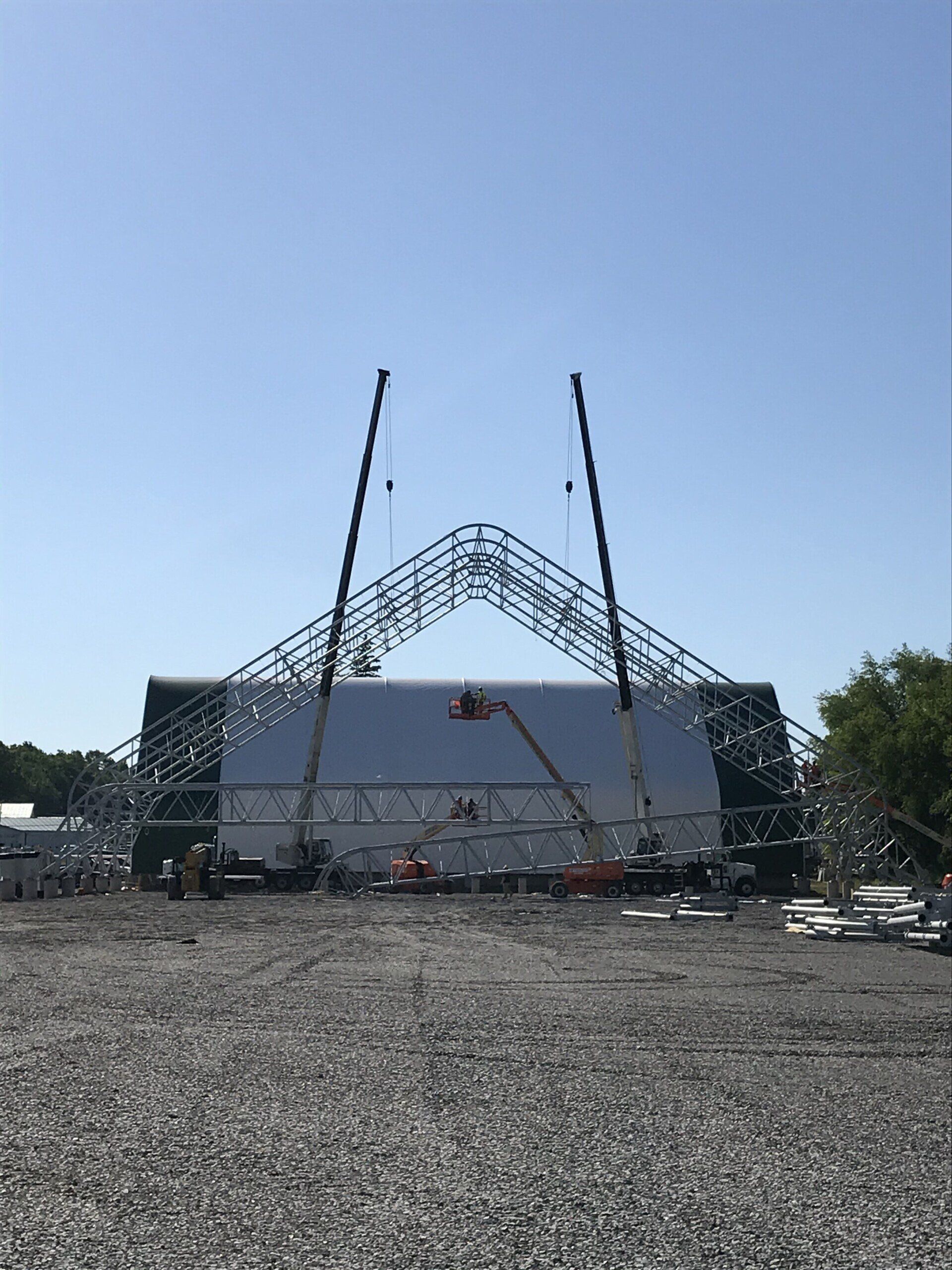 A large structure is being built in a gravel lot.