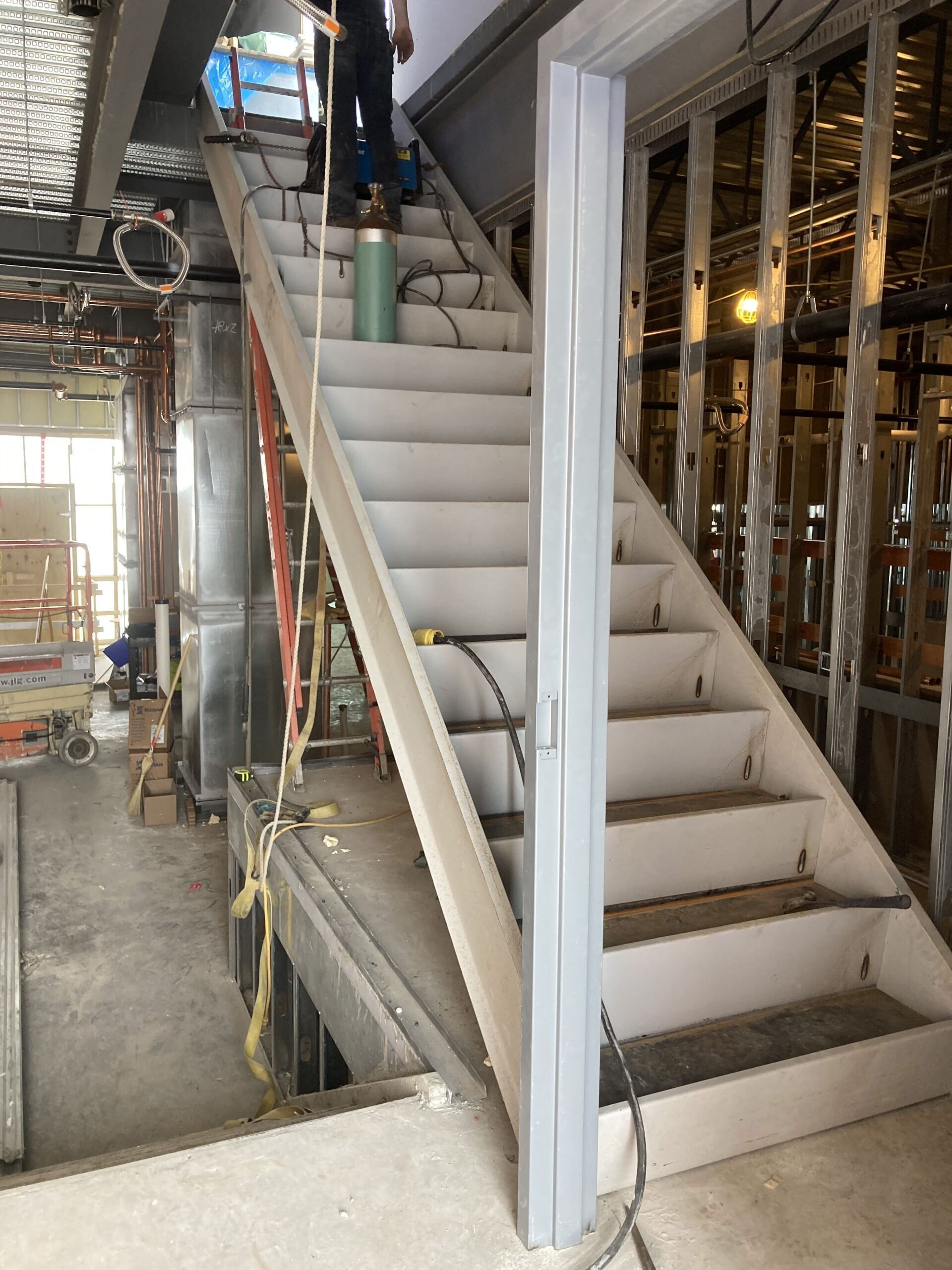 Staircase under construction; a person stands on the top. Gray, unfinished surroundings.