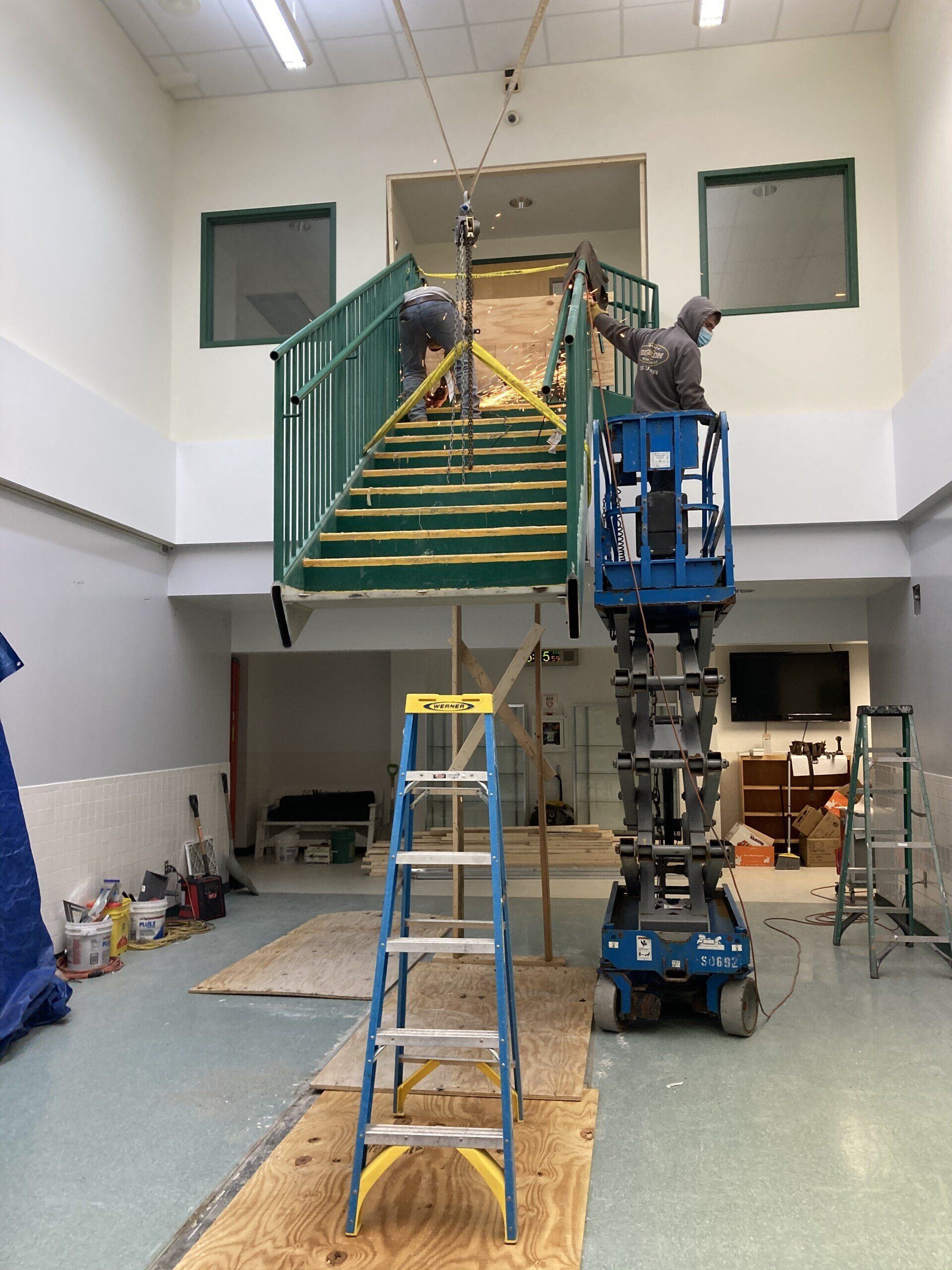 Workers on lift and staircase, renovating interior. One person works on stairs, the other on lift.