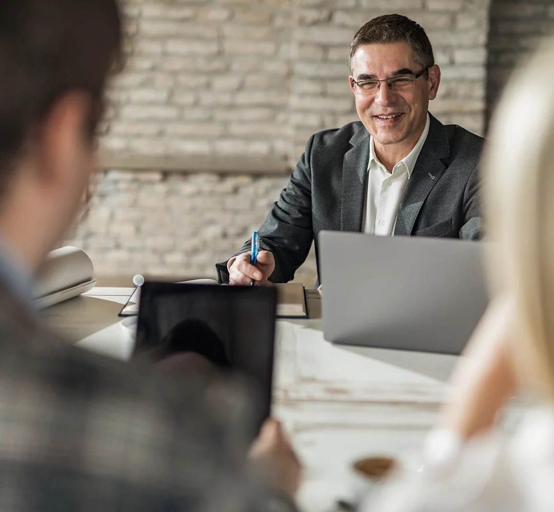 Business meeting with a smiling presenter at a laptop, seen across a conference table from colleagues