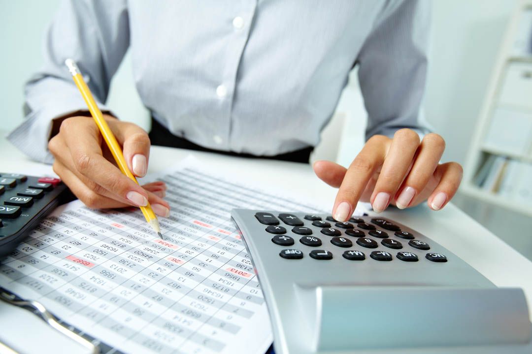 Hands using a calculator and pencil on financial paperwork beside a keyboard