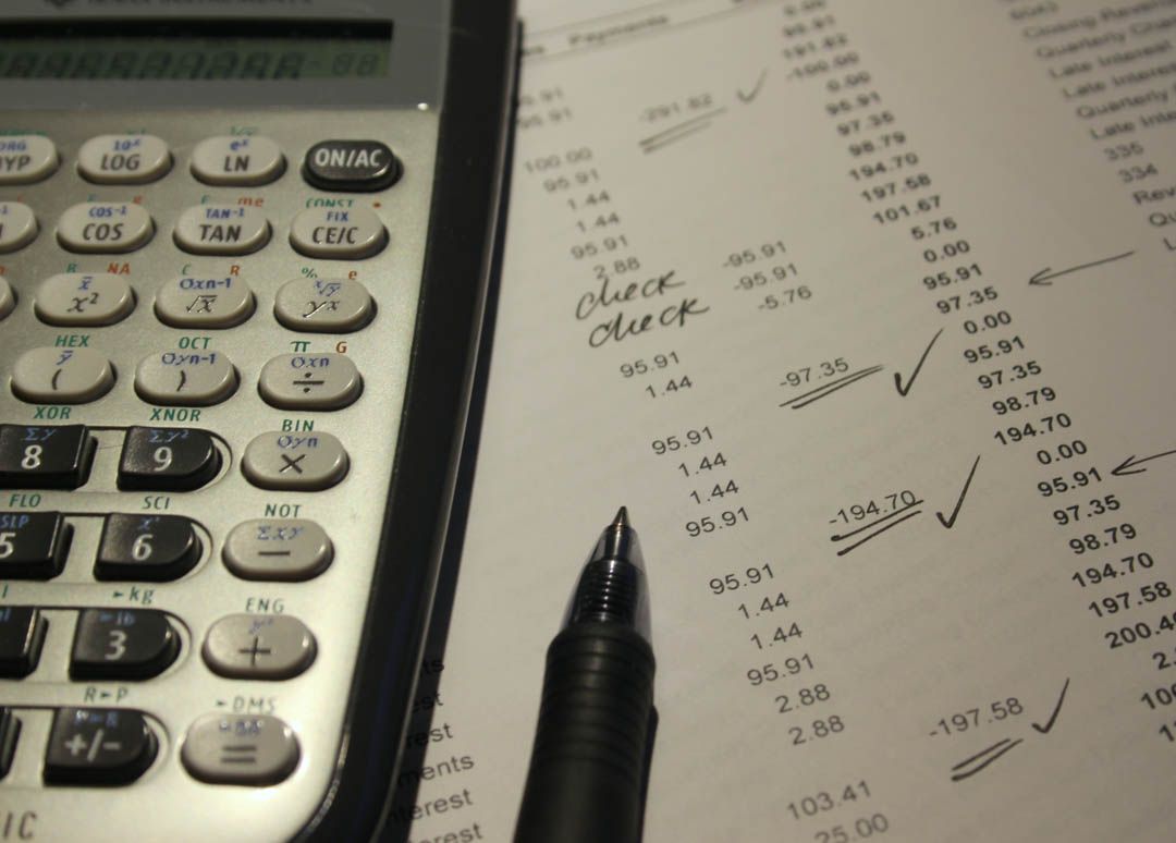Calculator, pen, and marked financial paperwork on a desk.