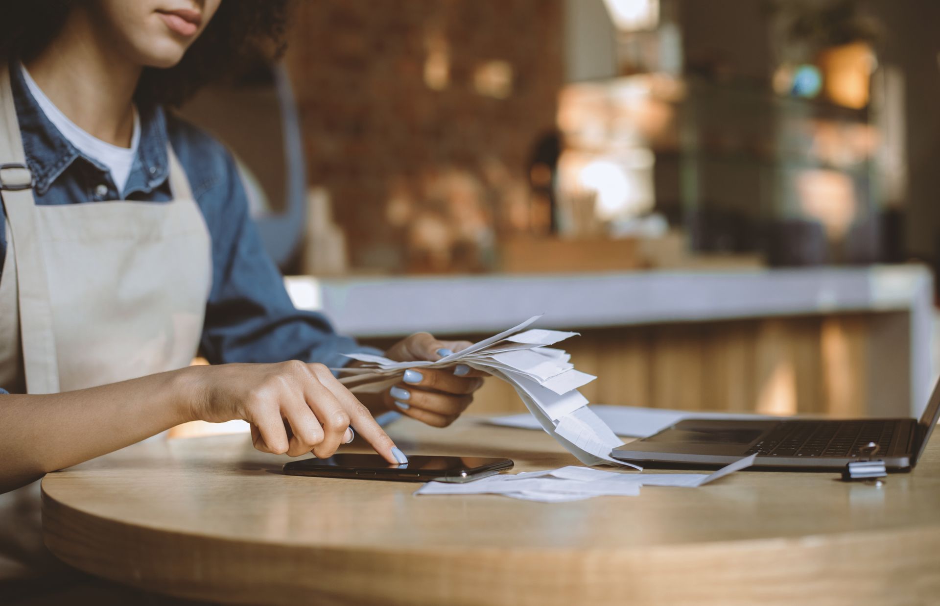 Person in an apron arranging papers and a silver model airplane at a wooden table in a café.