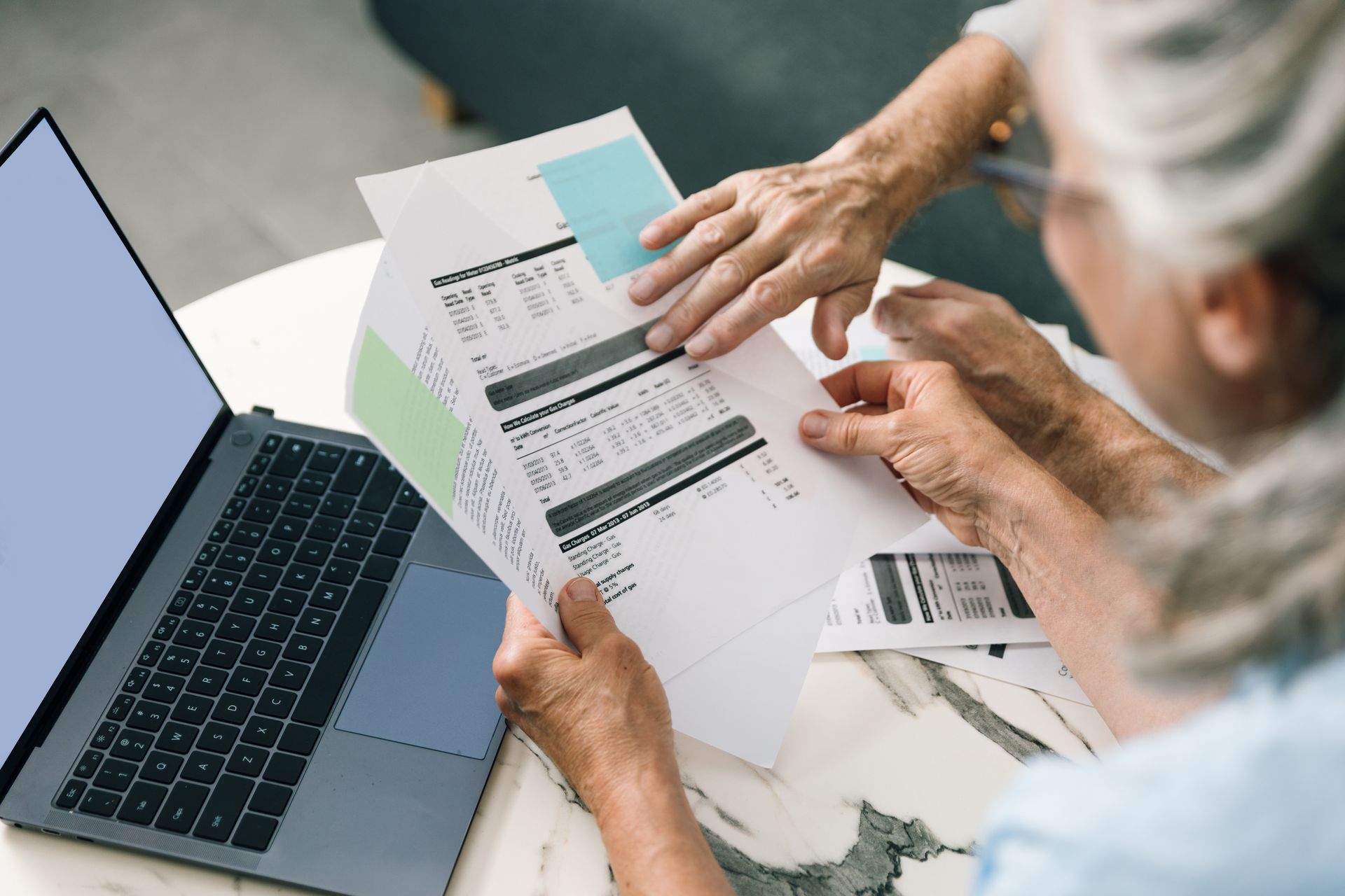Person reviewing printed documents beside a laptop on a desk