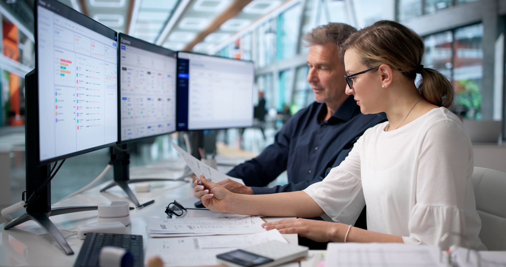 Two coworkers reviewing data on dual monitors in a bright office