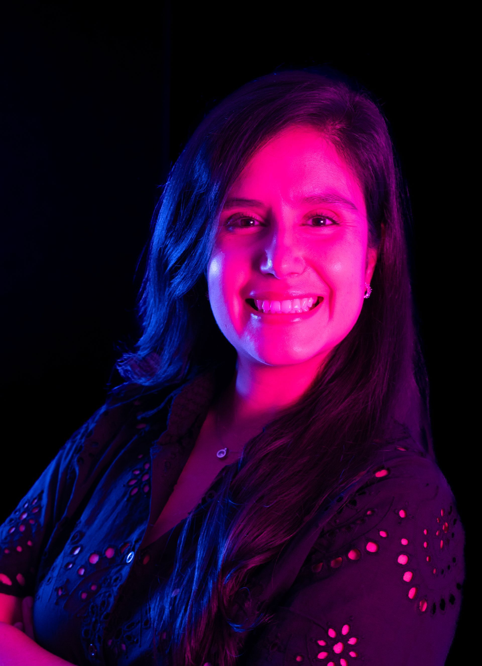 Portrait of a smiling person lit in vivid pink and blue against a dark background