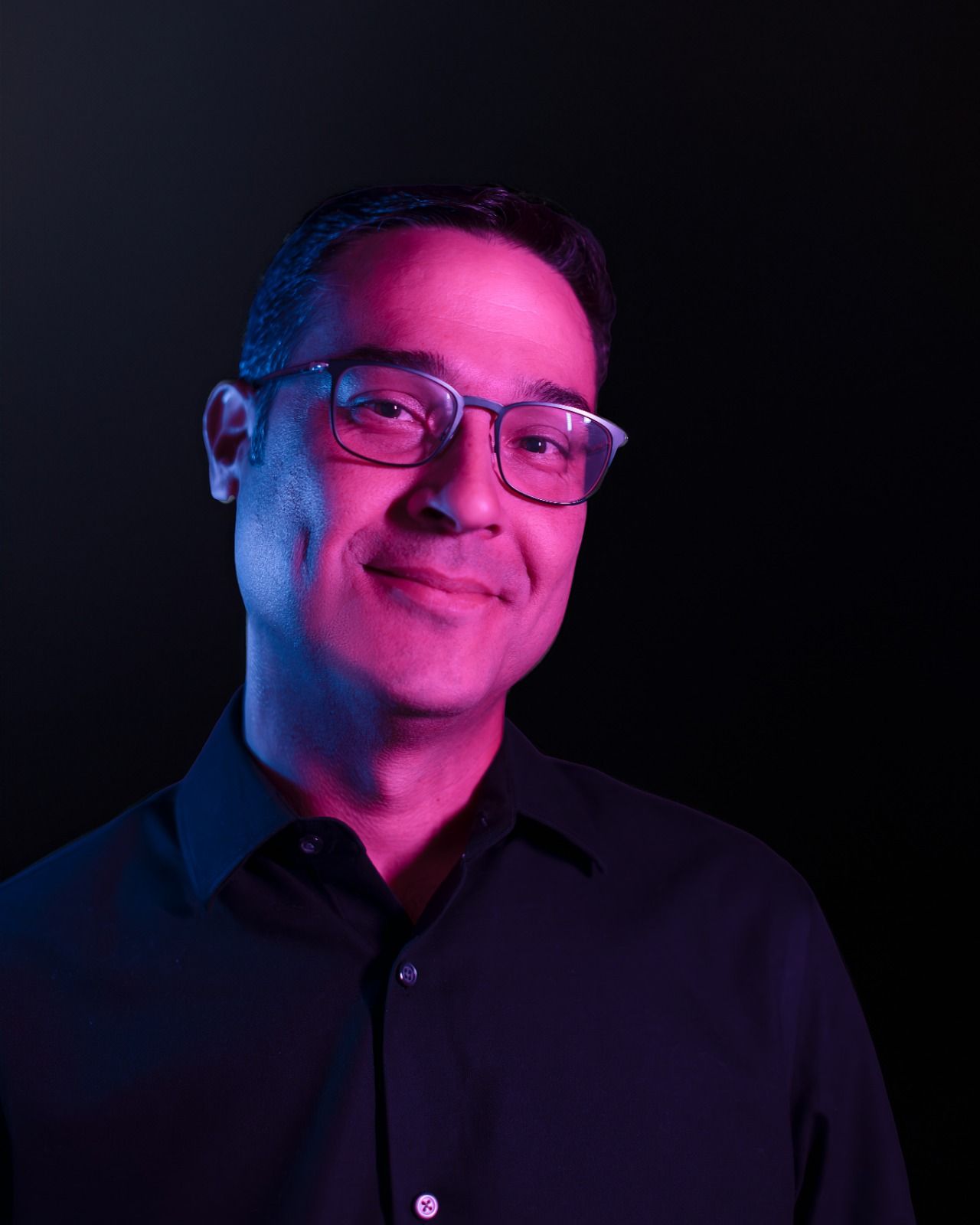Portrait of a smiling person with long hair under pink and blue studio lighting on a dark background