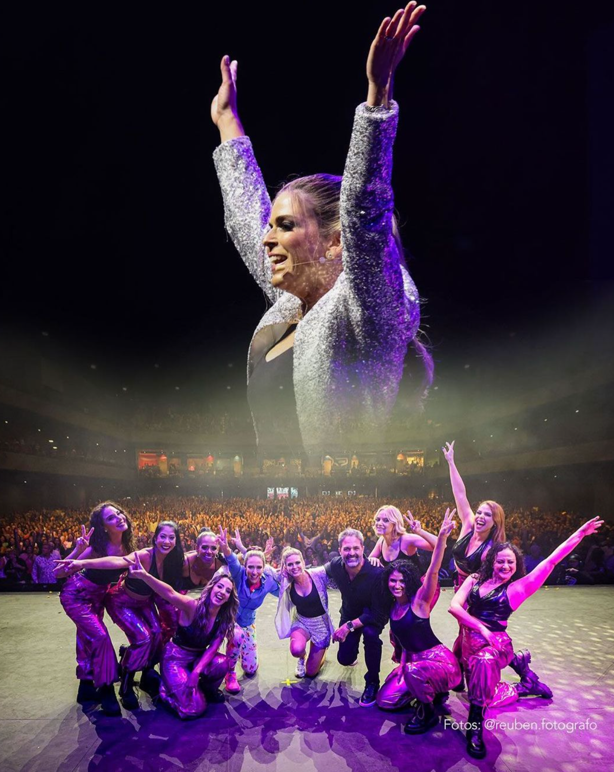 Dance troupe poses on stage beneath a large projected performer with arms raised.