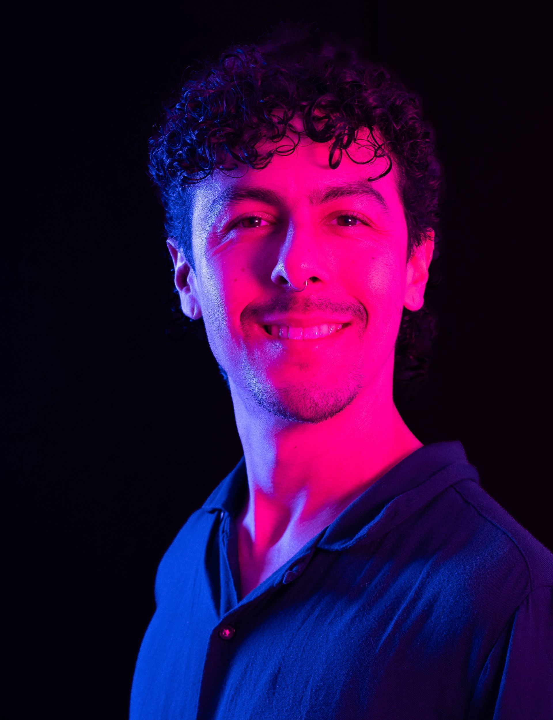 Smiling person lit in pink and blue against a black background