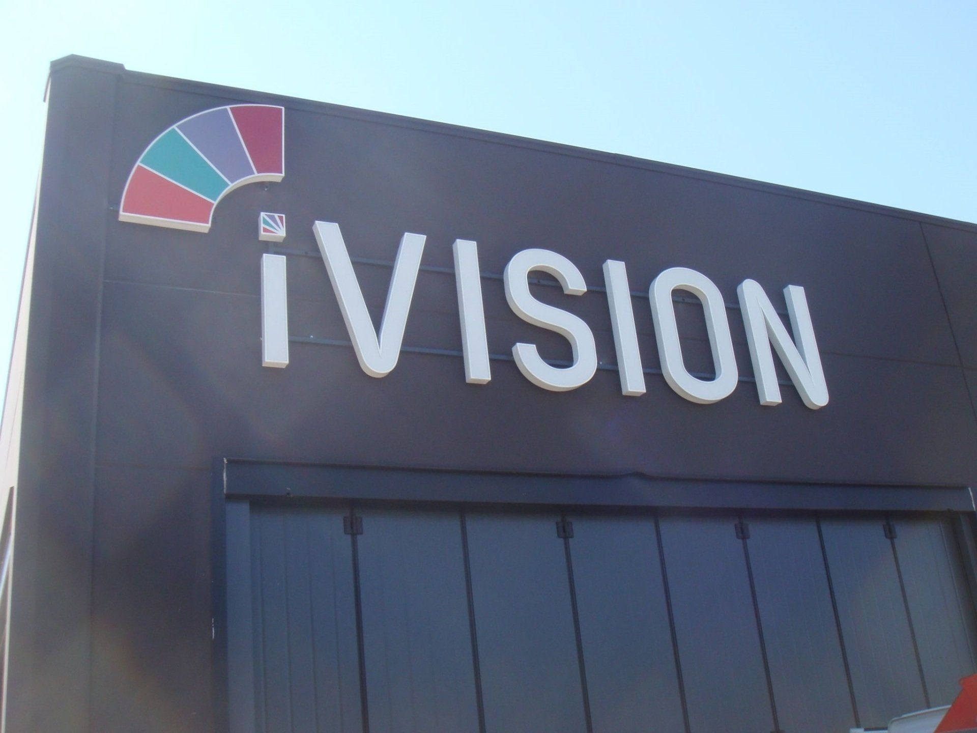 Insegna iVISION su una facciata scura di un edificio con un piccolo logo multicolore