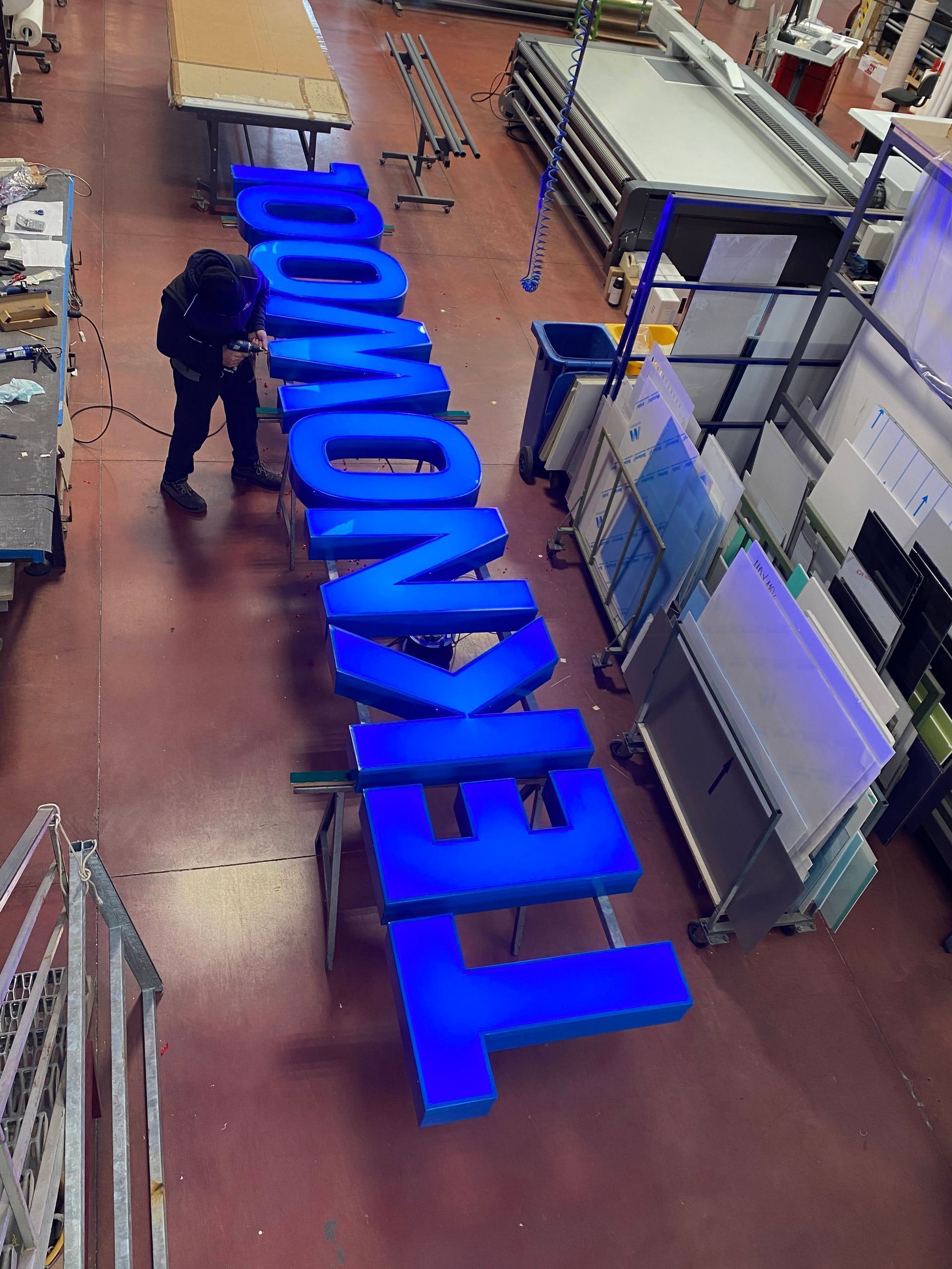 Un operaio sistema delle grandi lettere blu TEGNOVIS sul pavimento di una fabbrica.