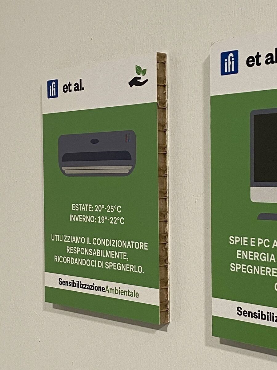 Due poster murali verdi con messaggi sul risparmio energetico e l'illustrazione di un condizionatore d'aria, esposti all'interno.