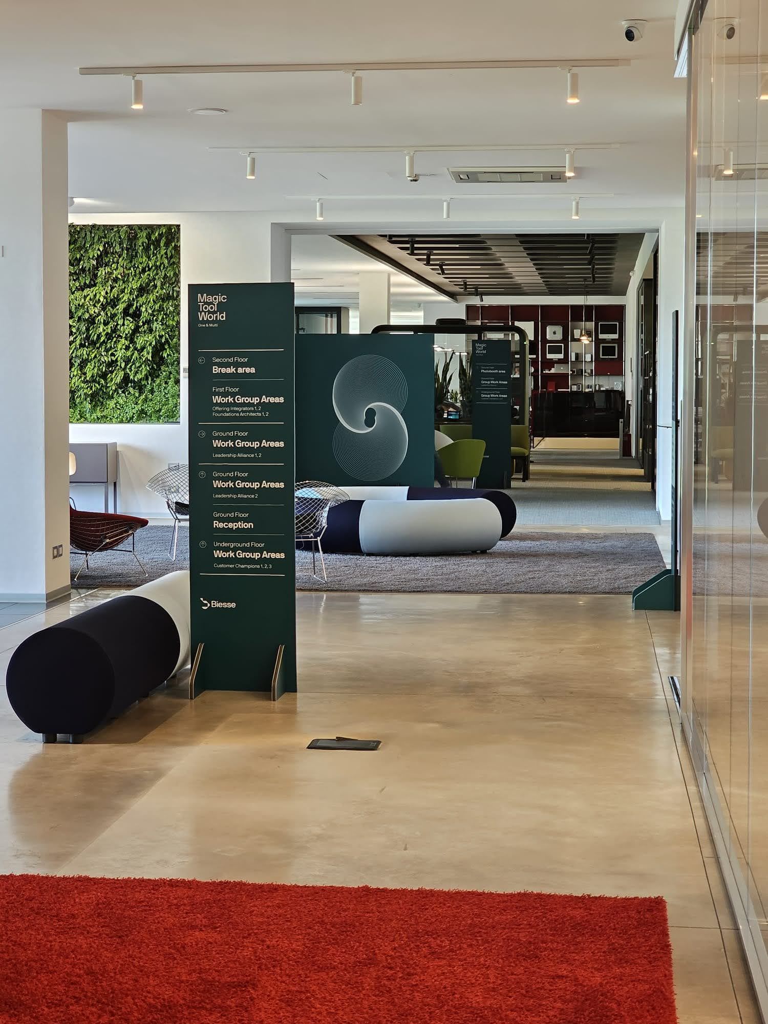 Hall moderna con moquette rossa e grigia, insegna verde e comode poltrone bianche.