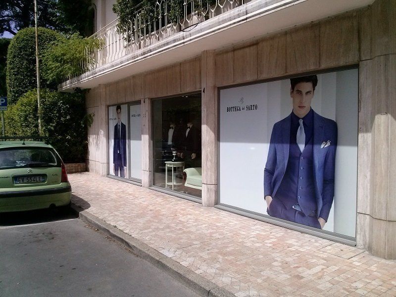 Marciapiede accanto a un negozio di abbigliamento con grandi poster di moda e un'auto verde parcheggiata all'esterno.