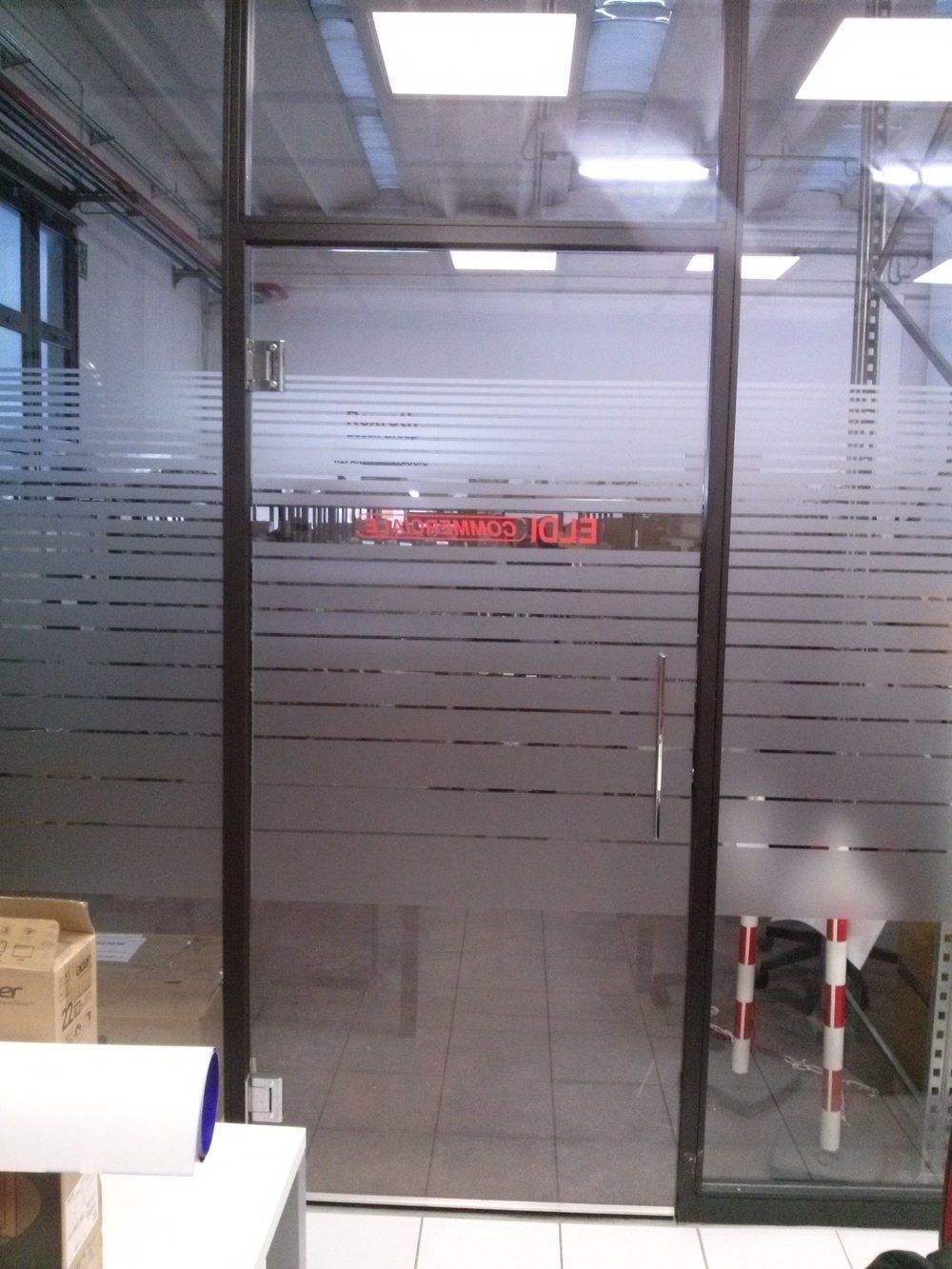 Porte di vetro da magazzino con strisce satinate, che lasciano intravedere scatole e scaffalature industriali all'interno.