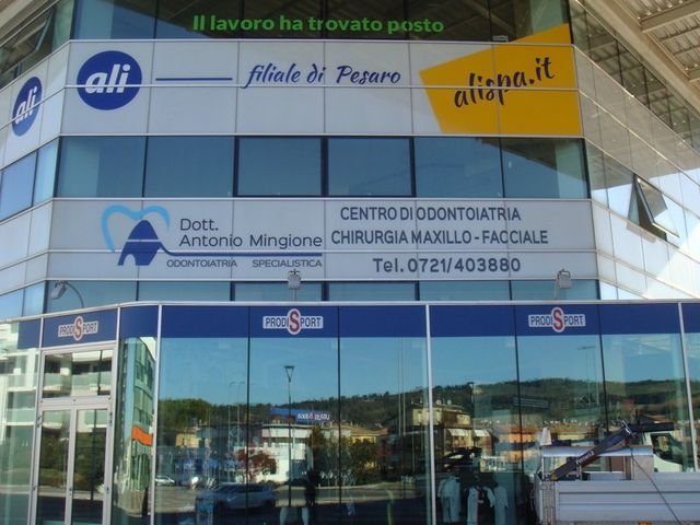 Edificio adibito a clinica odontoiatrica con facciata in vetro, insegne in italiano e colori blu e bianco.