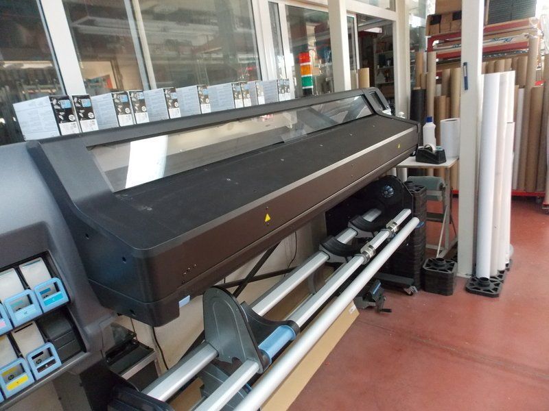 Stampante di grande formato in un'officina, con rotoli bianchi e attrezzature intorno.