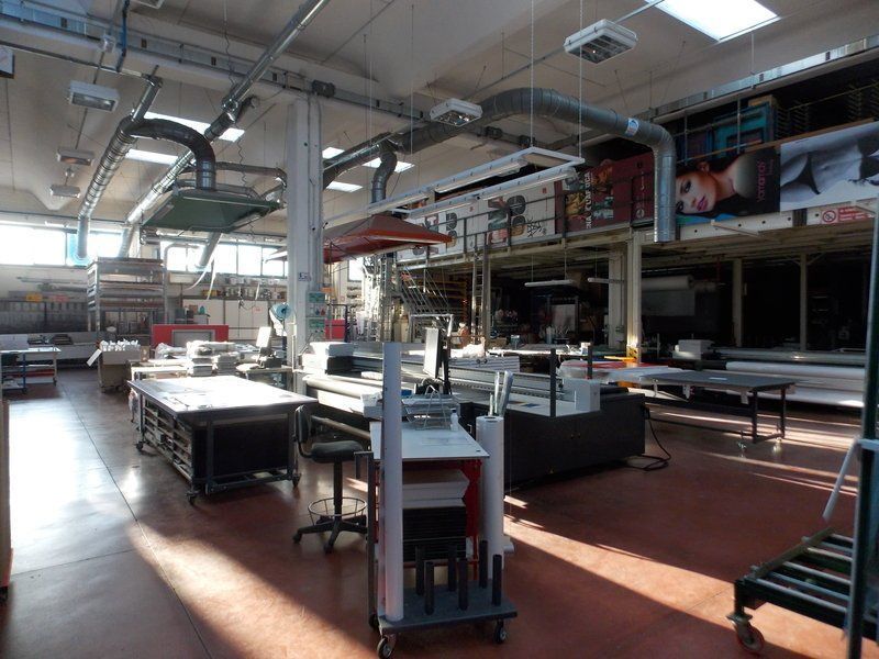 Spaziosa officina industriale con tavoli in metallo, macchinari e luce naturale che filtra attraverso le alte finestre.