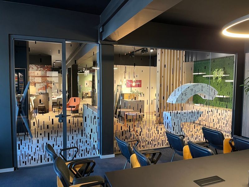 Una moderna sala relax per ufficio con pareti in vetro, sedie blu e un tavolo da conferenza vicino a una porta illuminata.